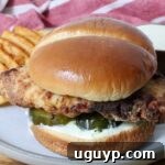 A crispy air fried chicken sandwich on a soft bun with pickles and creamy sauce, served with waffle fries on a plate.