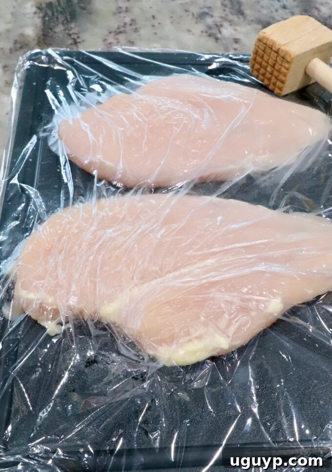 chicken breasts on a cutting board under a piece of plastic wrap