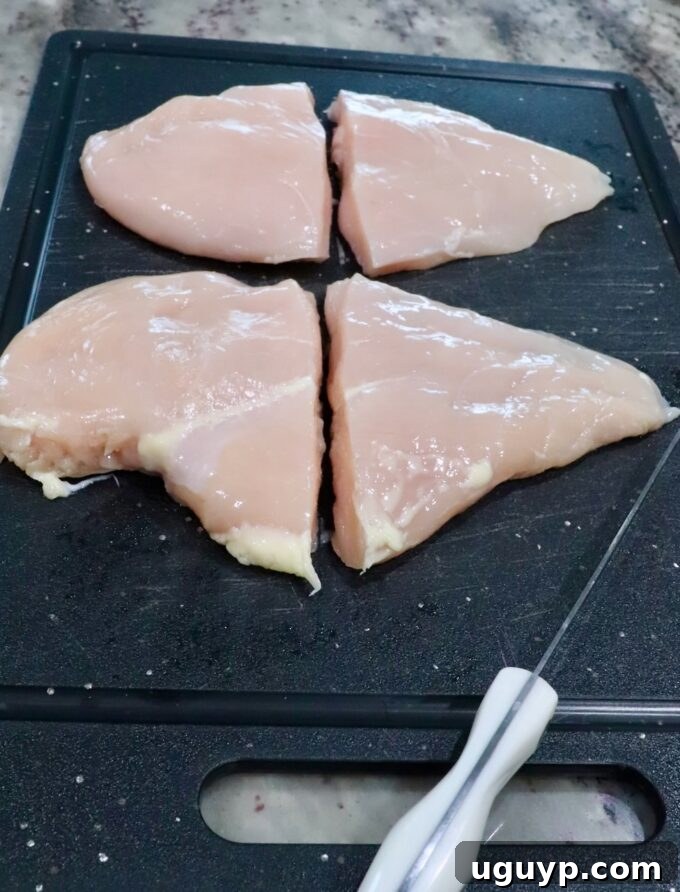 chicken breasts cut in half on a cutting board, sitting next to a knife