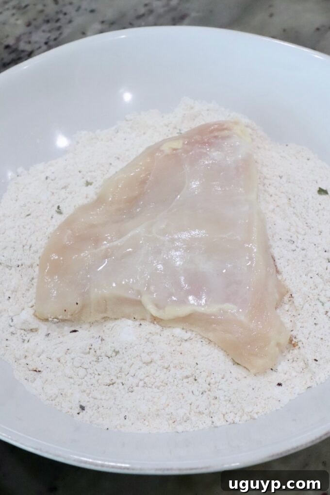 piece of chicken in a bowl of seasoned flour