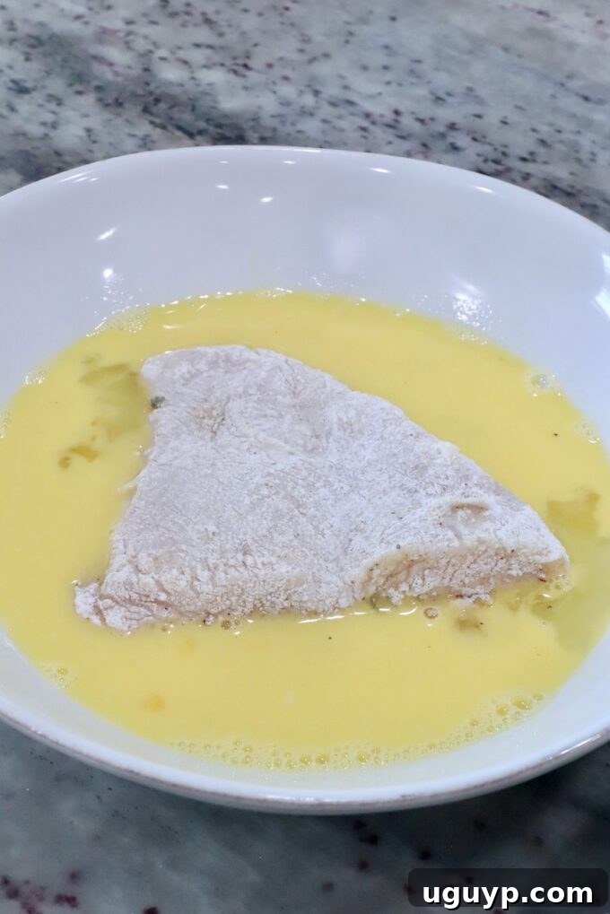 flour-coated chicken in a bowl of whisked eggs