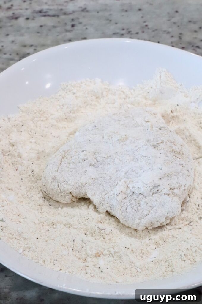 a piece of coated chicken in a bowl of flour