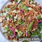 A vibrant salad with greens, quinoa, chickpeas, sliced almonds, carrots, and pickled onions on a plate with a fork, ready to be enjoyed.