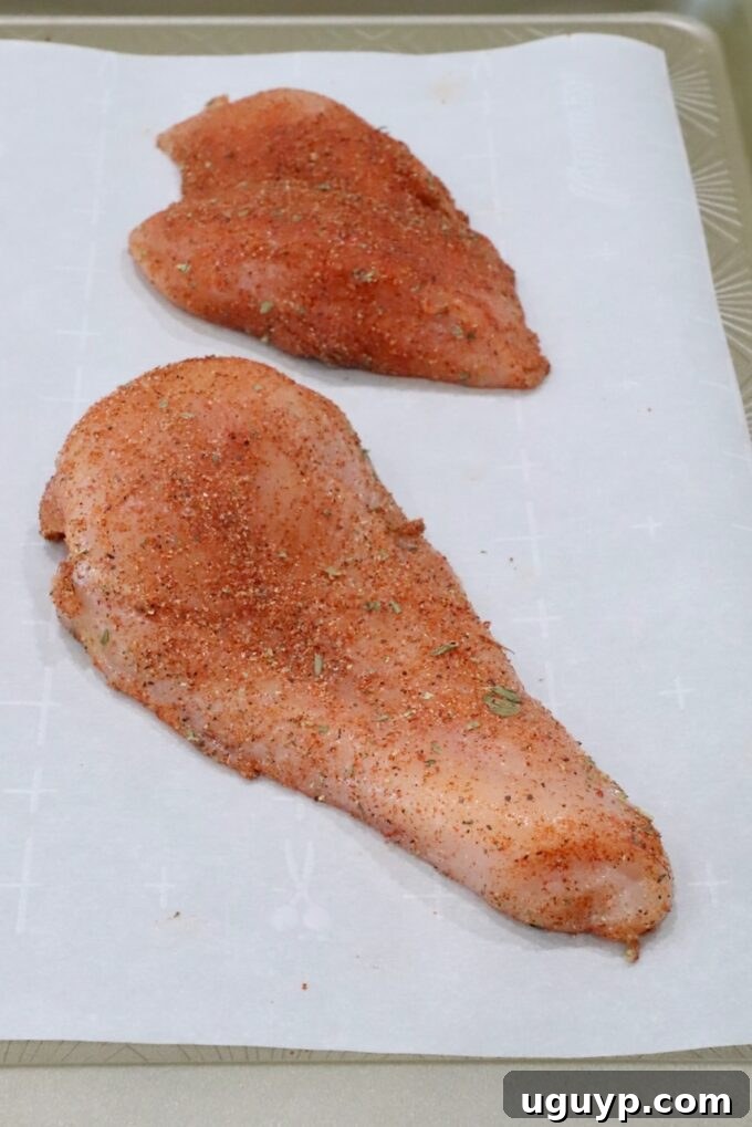 Seasoned chicken breasts on a parchment-lined baking sheet, prepared for roasting.