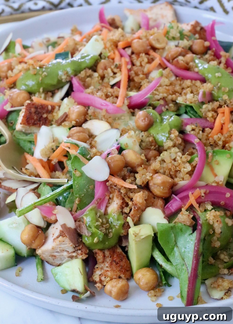 A vibrant salad with greens, quinoa, chickpeas, sliced almonds, carrots, and pickled onions on a plate, showcasing its appetizing appeal.