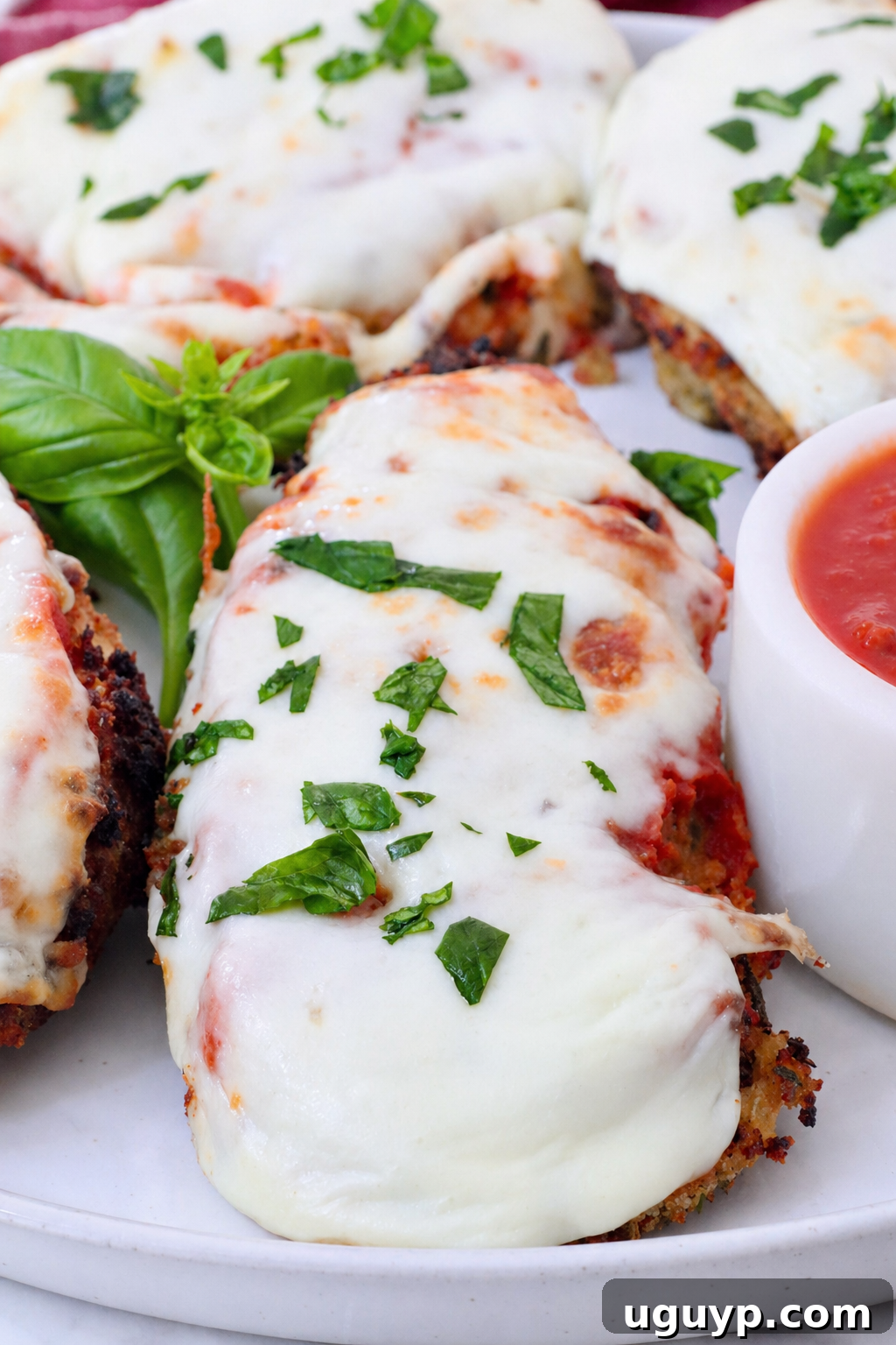 Crispy pieces of Air Fryer Chicken Parmesan on a plate, garnished with fresh basil, accompanied by a small bowl of marinara sauce.