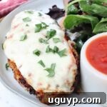 Melted mozzarella over chicken on a plate, garnished with fresh basil, with a side salad and small bowl of marinara sauce
