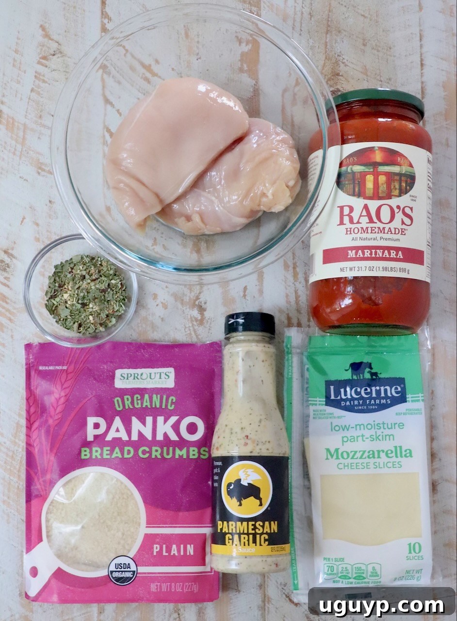 Ingredients for Air Fryer Chicken Parmesan laid out on a wooden surface: raw chicken breasts, marinara sauce jar, panko bread crumbs, Parmesan garlic dressing, mozzarella cheese slices, and a small bowl of fresh herbs.