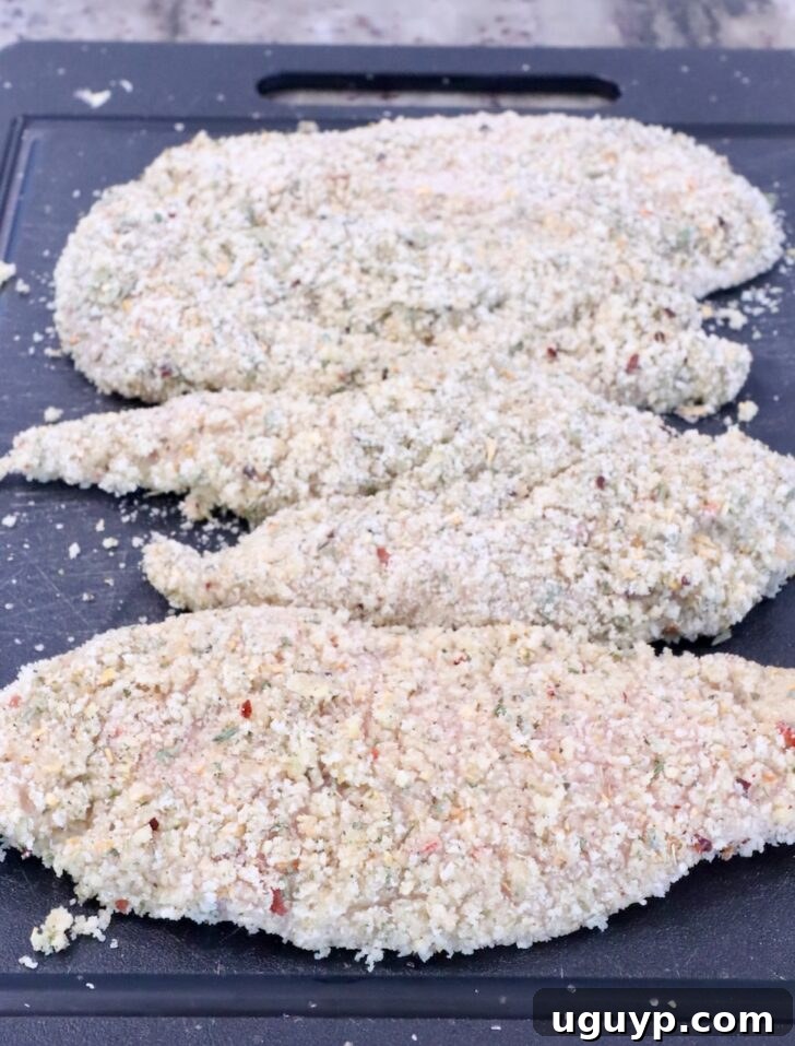 Breaded chicken breasts arranged neatly on a black cutting board, ready for the air fryer.