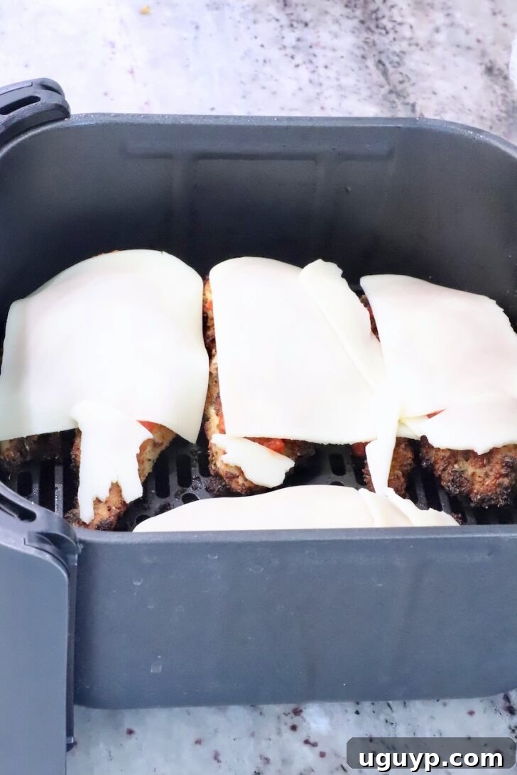 Mozzarella cheese slices perfectly melted over marinara-covered crispy chicken breasts in the air fryer, glistening with warmth.