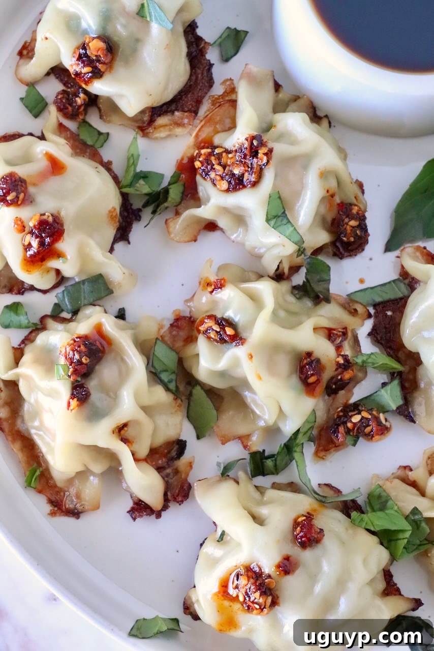 cooked blanket dumplings on a plate topped with thai basil and chili crisp, with a small bowl of dipping sauce on the side