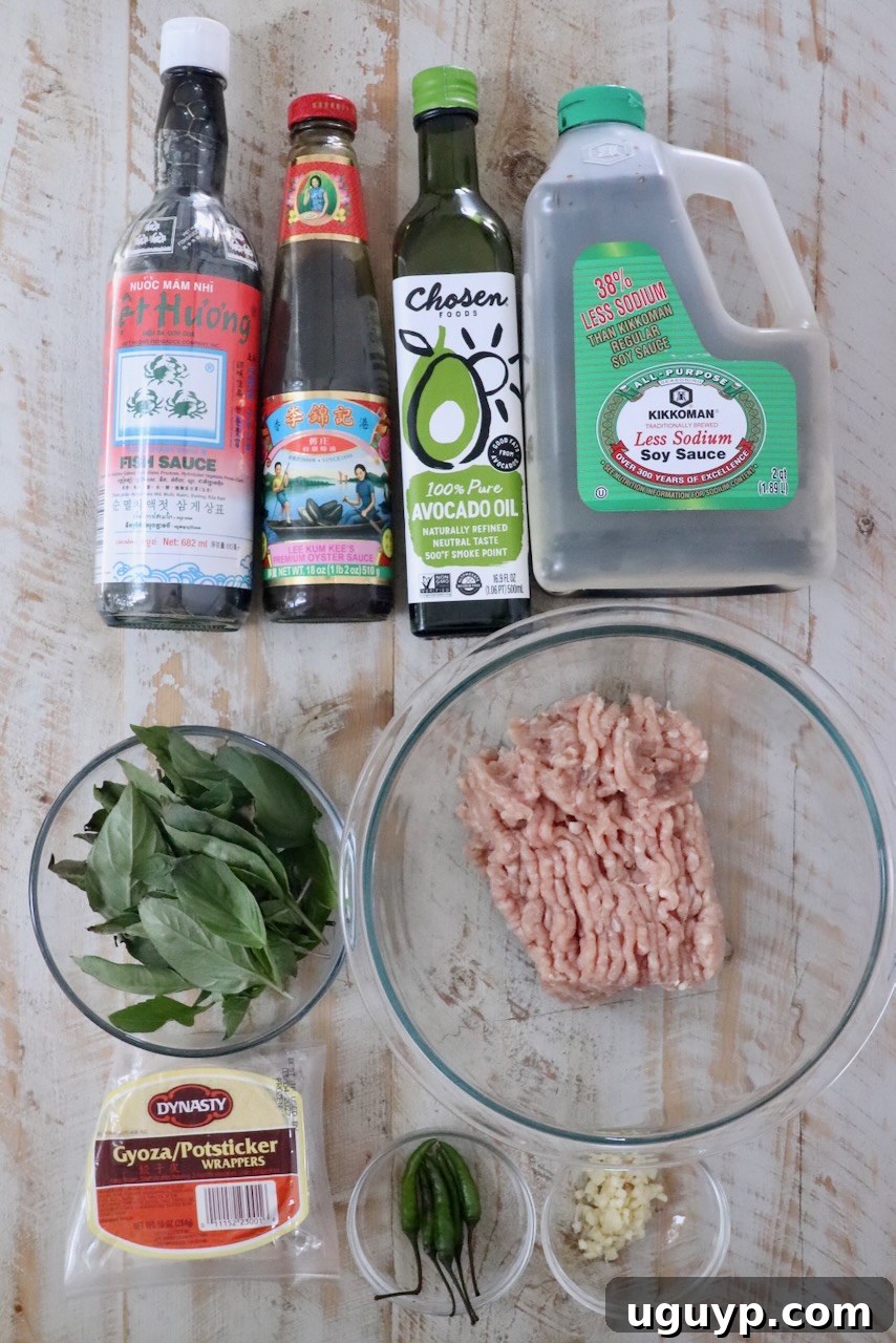 Assorted cooking ingredients on a wooden surface, including fish sauce, oyster sauce, avocado oil, soy sauce, ground chicken, Thai basil, dumpling wrappers, chili peppers, and minced garlic.