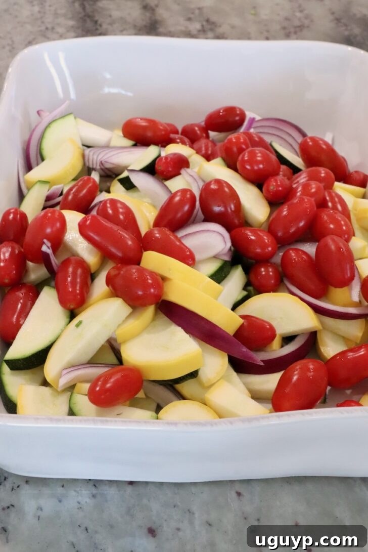 sliced yellow squash, zucchini, asparagus and onions in a large baking dish with cherry tomatoes