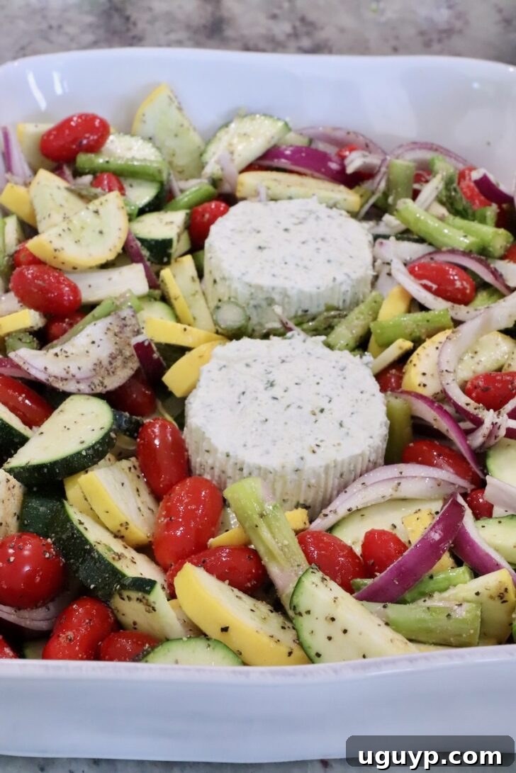 A white dish filled with vibrant chopped vegetables, including cherry tomatoes, zucchini, squash, and red onion, surrounds two seasoned cheese rounds.