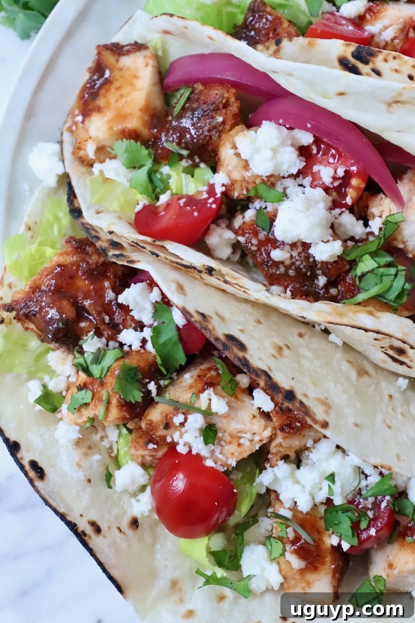air fryer chicken tacos topped with diced tomatoes, pickled onions, cilantro, lettuce, and crumbled cheese on lightly charred tortillas.