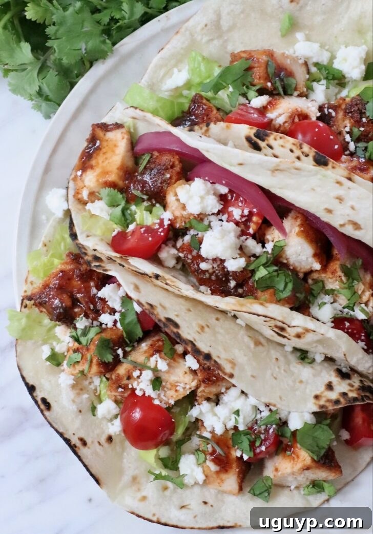 air fryer chicken tacos topped with diced tomatoes, pickled onions, cilantro, lettuce, and crumbled cheese on lightly charred tortillas.