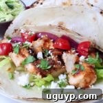 air fryer chicken tacos topped with diced tomatoes, pickled onions, cilantro, lettuce, and crumbled cheese on lightly charred tortillas.