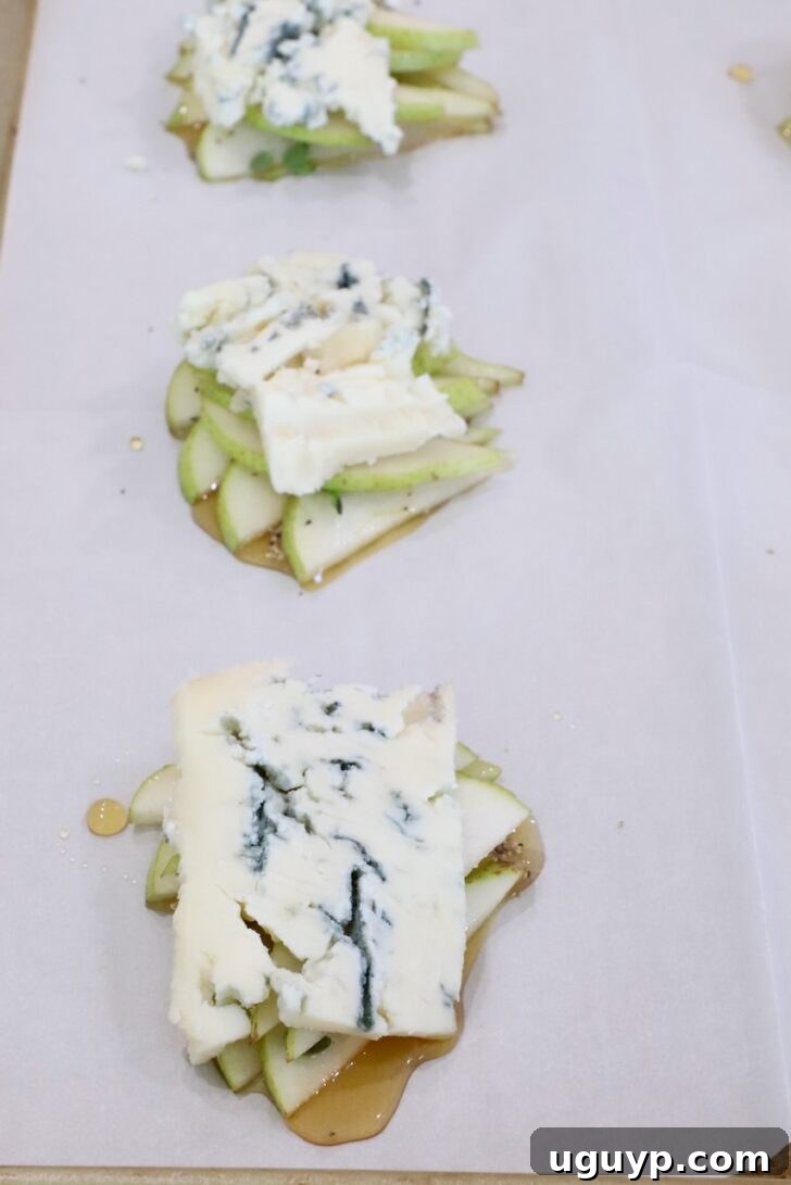 slices of gorgonzola cheese on top of sliced pears and honey on a sheet of parchment paper on a baking sheet