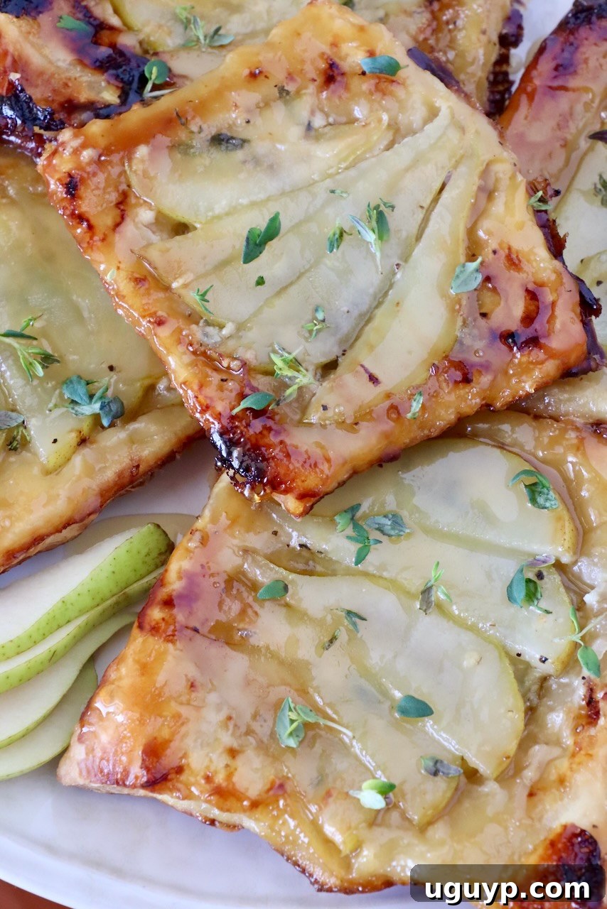 Golden brown pear tarts topped with fresh thyme, placed on a white plate.