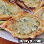 Close-up of golden-brown puff pastry tarts topped with sliced pears and drizzled with honey, garnished with fresh thyme leaves.