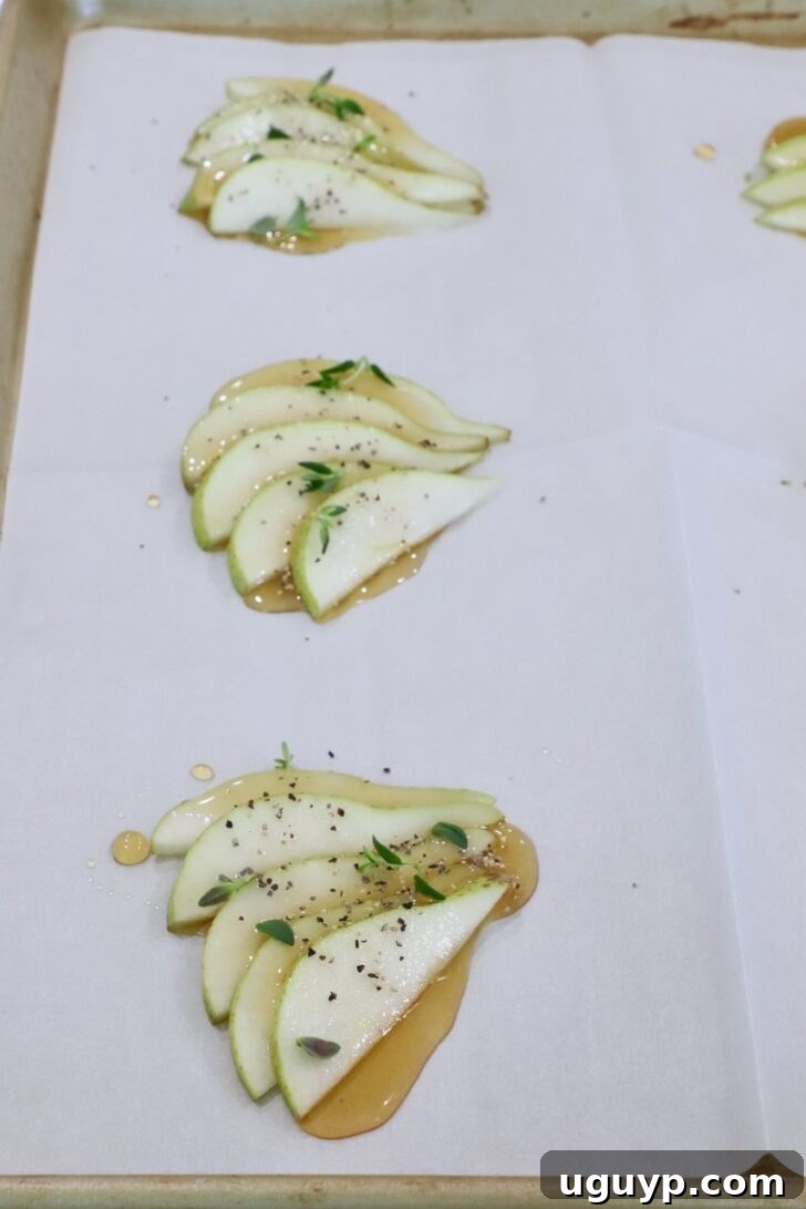 sliced pears topped with honey, salt, pepper, and fresh thyme, on a sheet of parchment paper on a baking sheet 