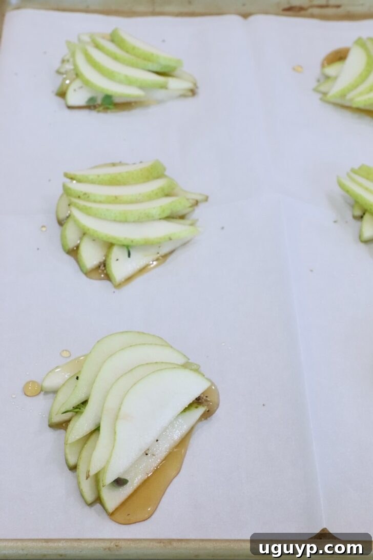 sliced pears stacked up  on a parchment-lined baking sheet