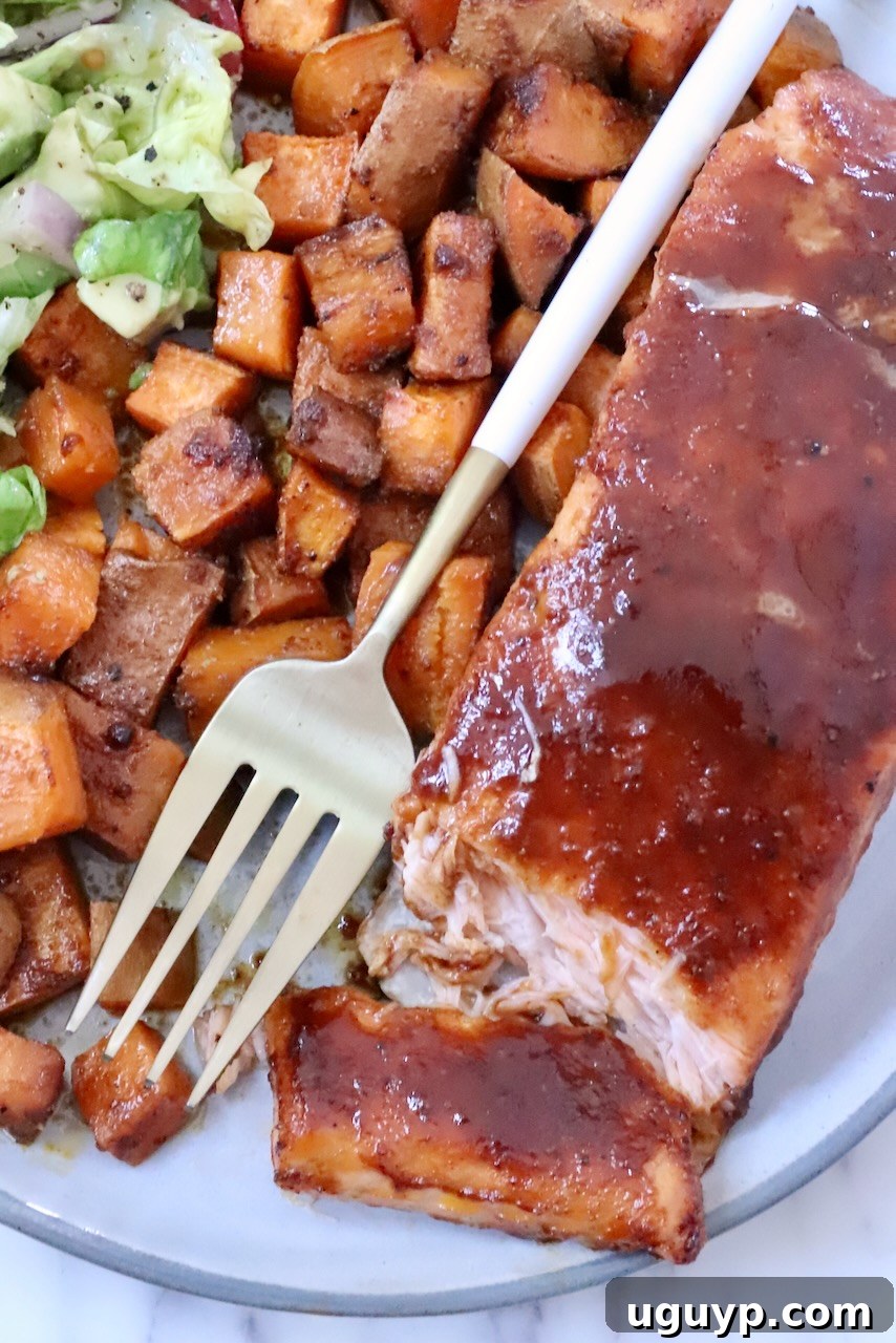 A plate of glazed salmon fillet, accompanied by seasoned sweet potato cubes and a side salad. A gold fork rests on the plate.