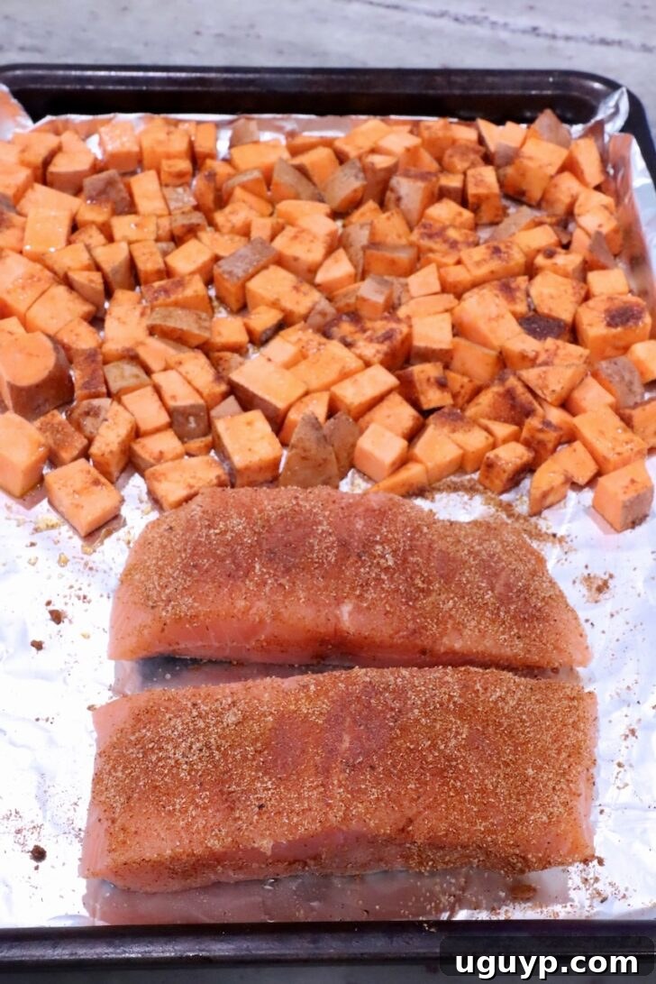 diced seasoned sweet potatoes on a foil lined baking sheet with two pieces of seasoned salmon filets
