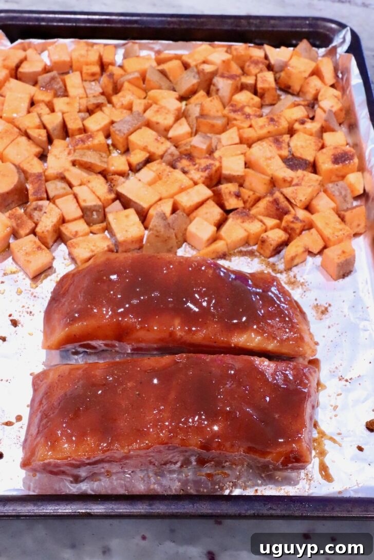 diced seasoned sweet potatoes on a foil lined baking sheet with two salmon filets coated in bbq sauce