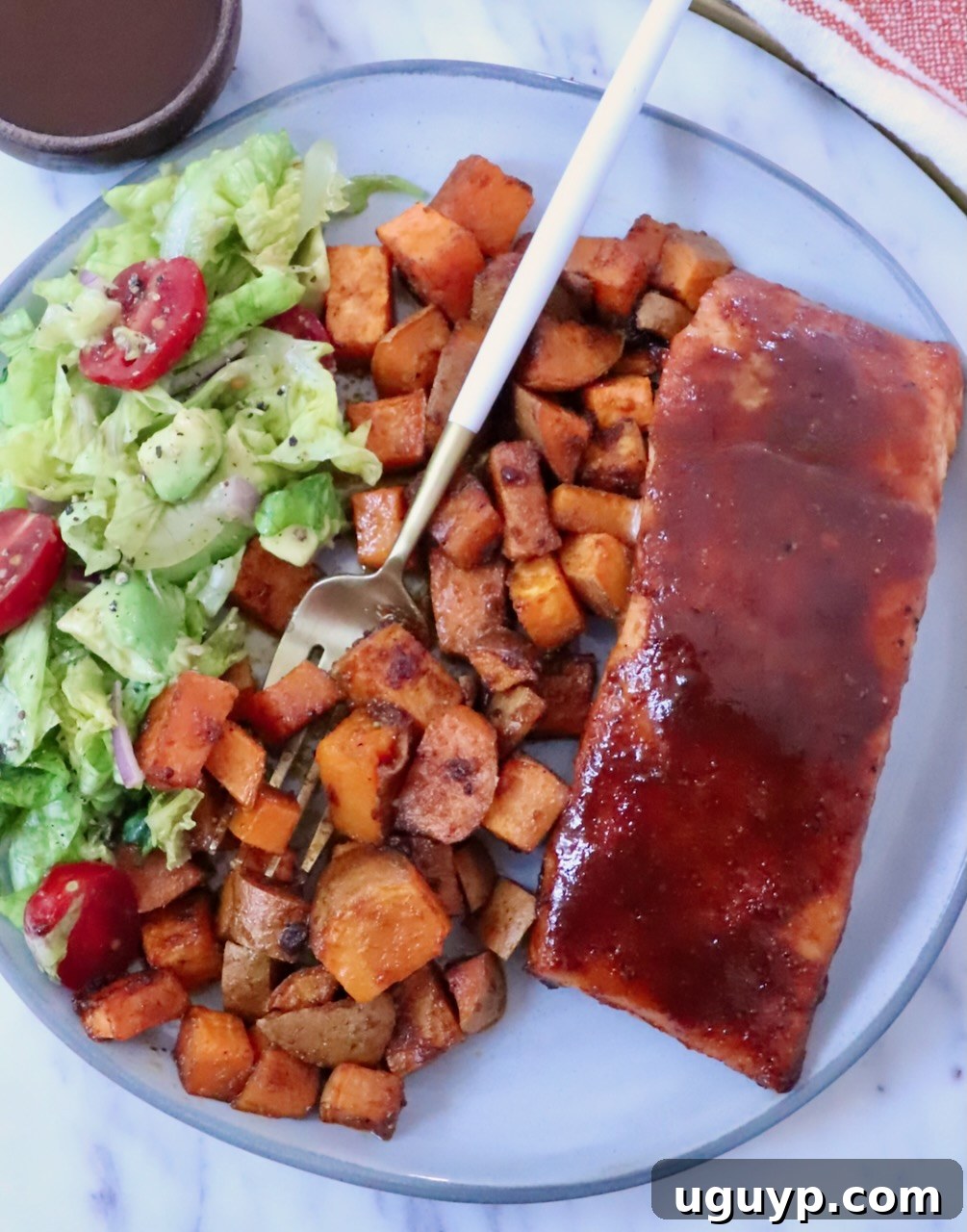 BBQ glazed salmon on a plate with roasted sweet potatoes, a side salad, and a fork