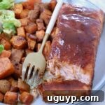 A plate of glazed salmon fillet, accompanied by seasoned sweet potato cubes and a side salad. A gold fork rests on the plate.