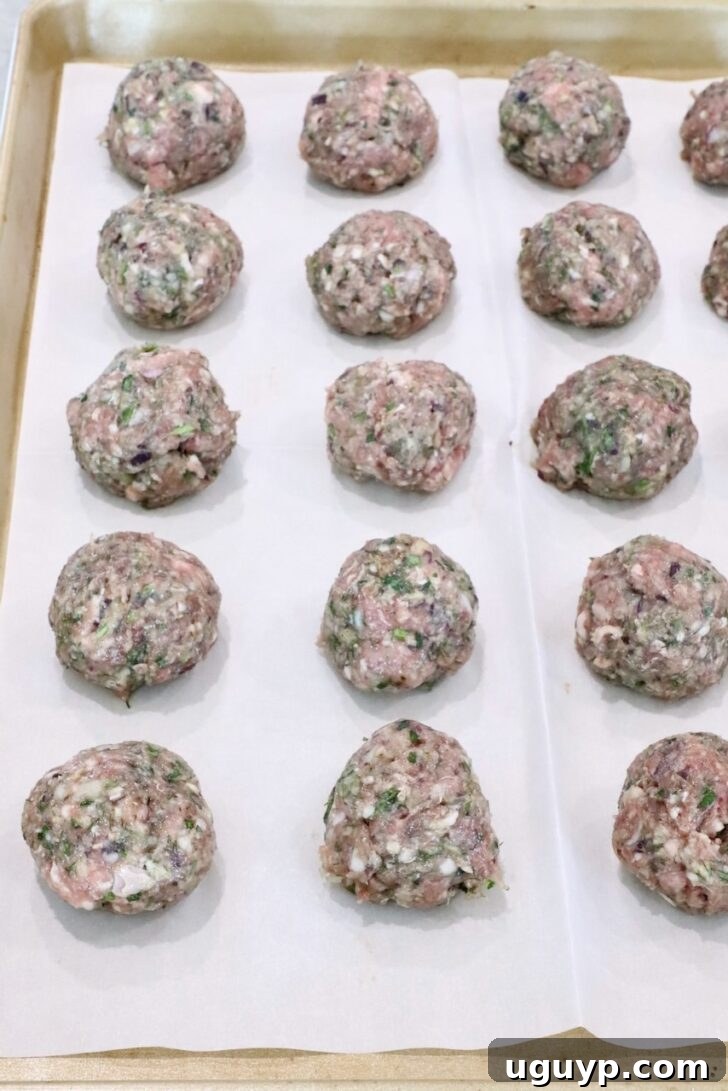 Raw meatballs arranged in rows on a parchment-lined baking sheet.