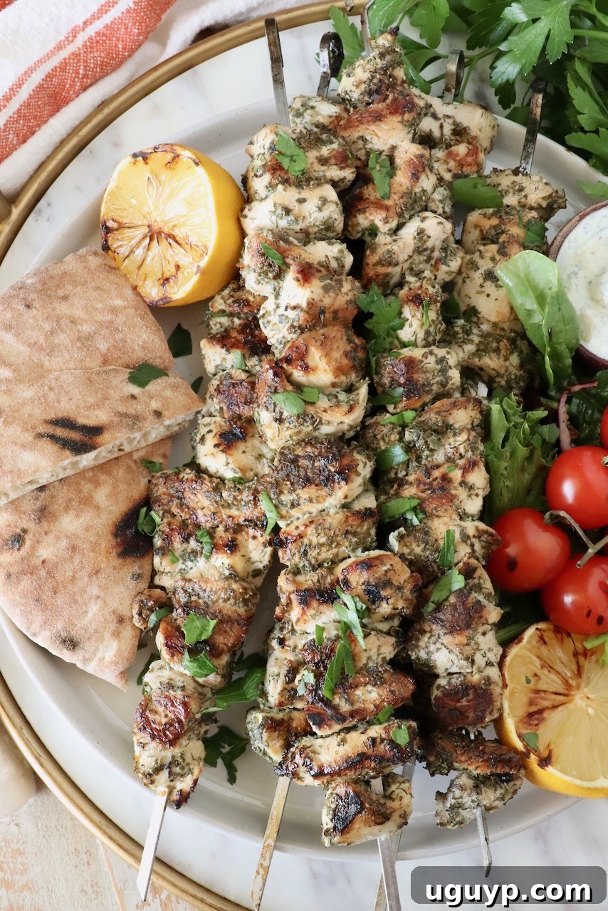 chicken souvlaki on skewers stacked up on a plate next to grilled pita bread, lemons and tomatoes