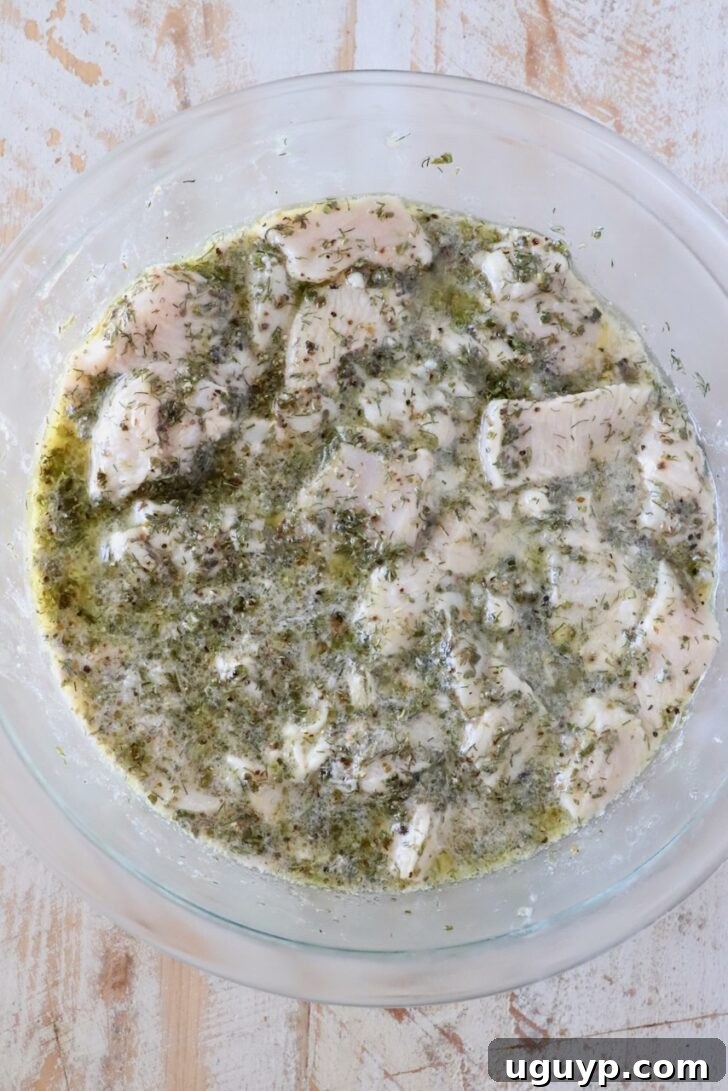 cubes of raw chicken in a lemon herb marinade in a glass bowl