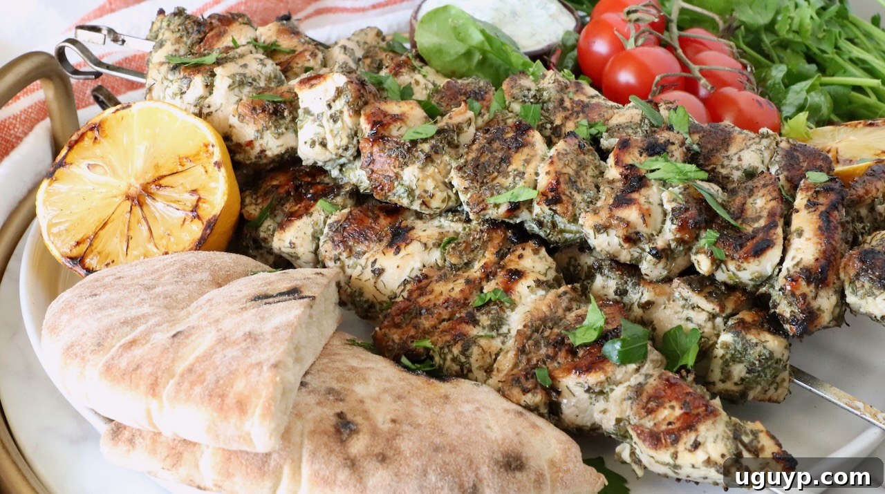 grilled chicken skewers on a plate with pita bread, grilled lemons, tomatoes and herbs