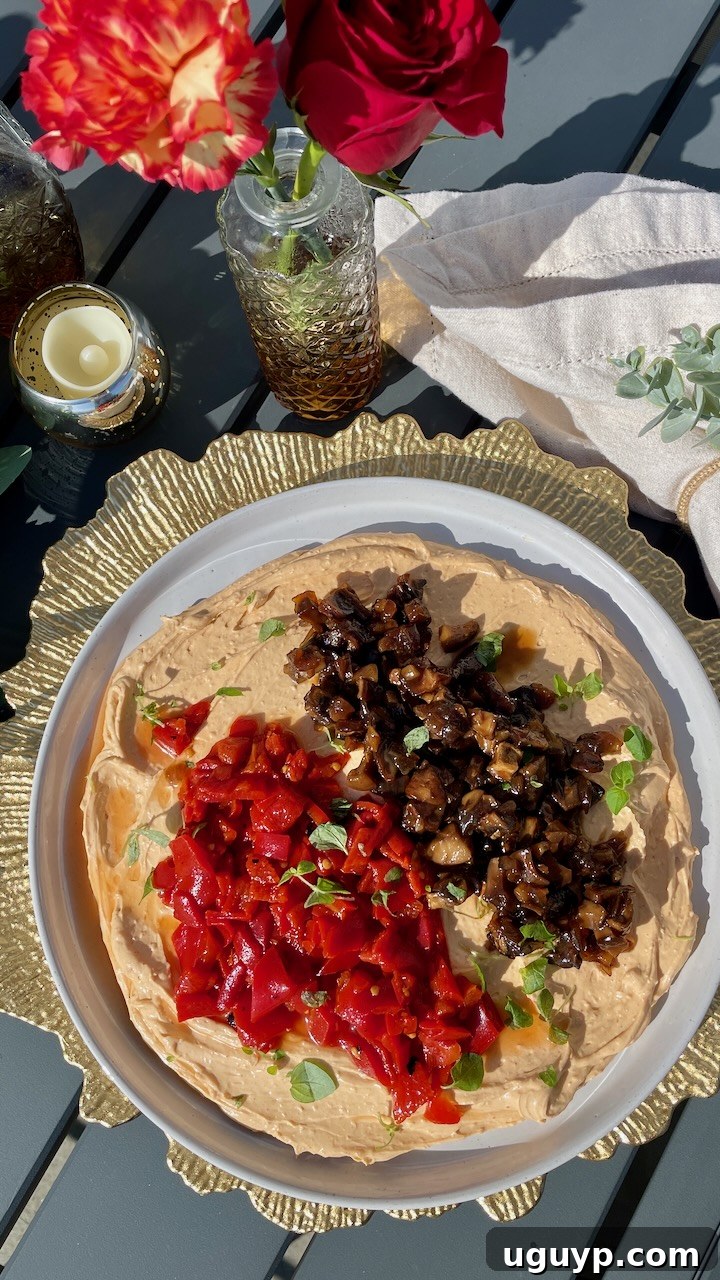whipped goat cheese on a plate topped with mushroom jam and diced roasted peppers, with flowers and a candle on the side of the plate