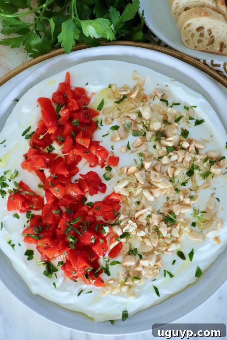whipped goat cheese dip on a rimmed plate topped with chopped almonds, roasted red peppers and fresh herbs