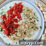 creamy goat cheese dip on a plate topped with chopped almonds, roasted red peppers, and fresh parsley, with a sliced baguette on the side