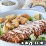 sliced blackened chicken on top of a salad in a bowl with croutons and grated parmesan cheese