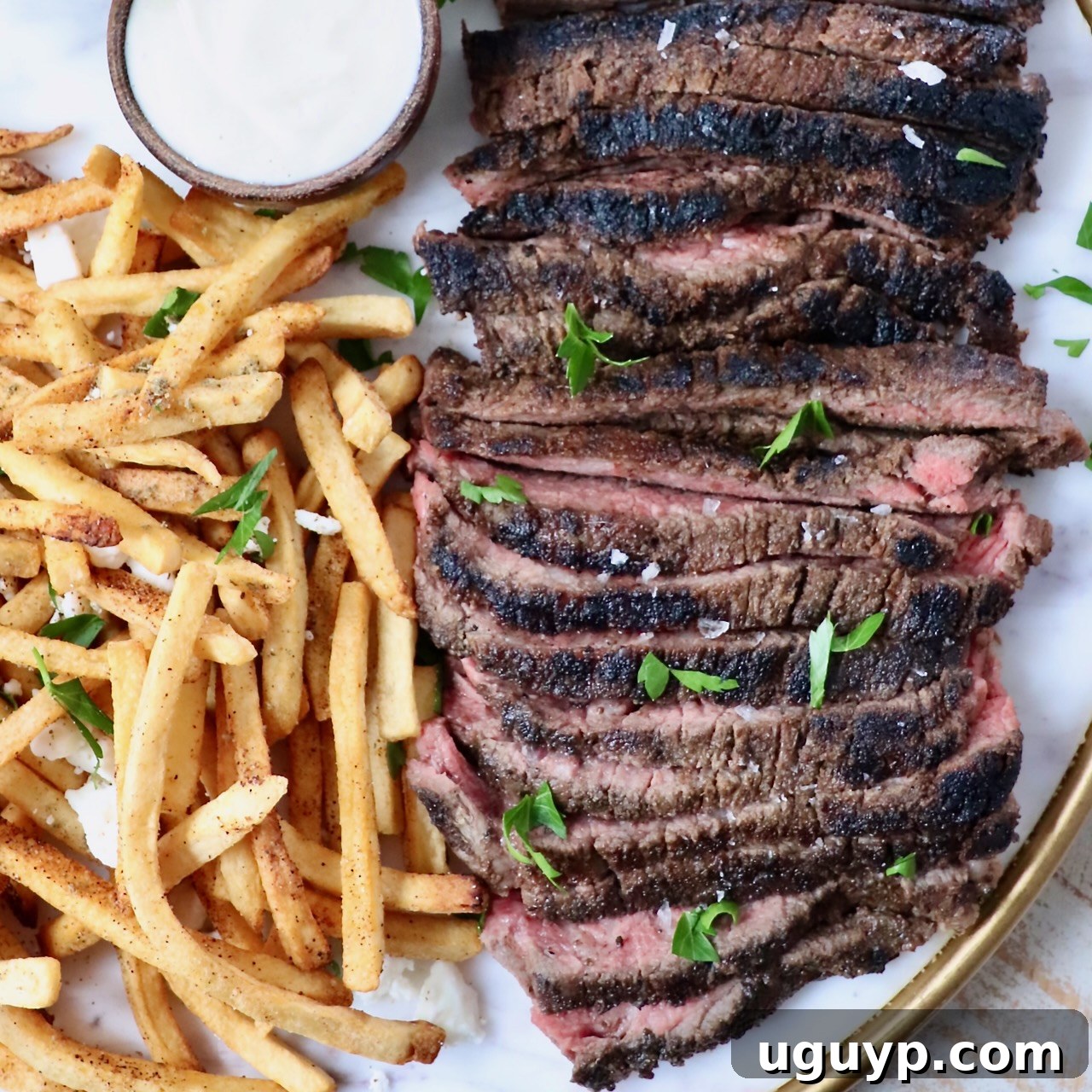 sliced steak on a platter next to french fries and a small bowl of sauce