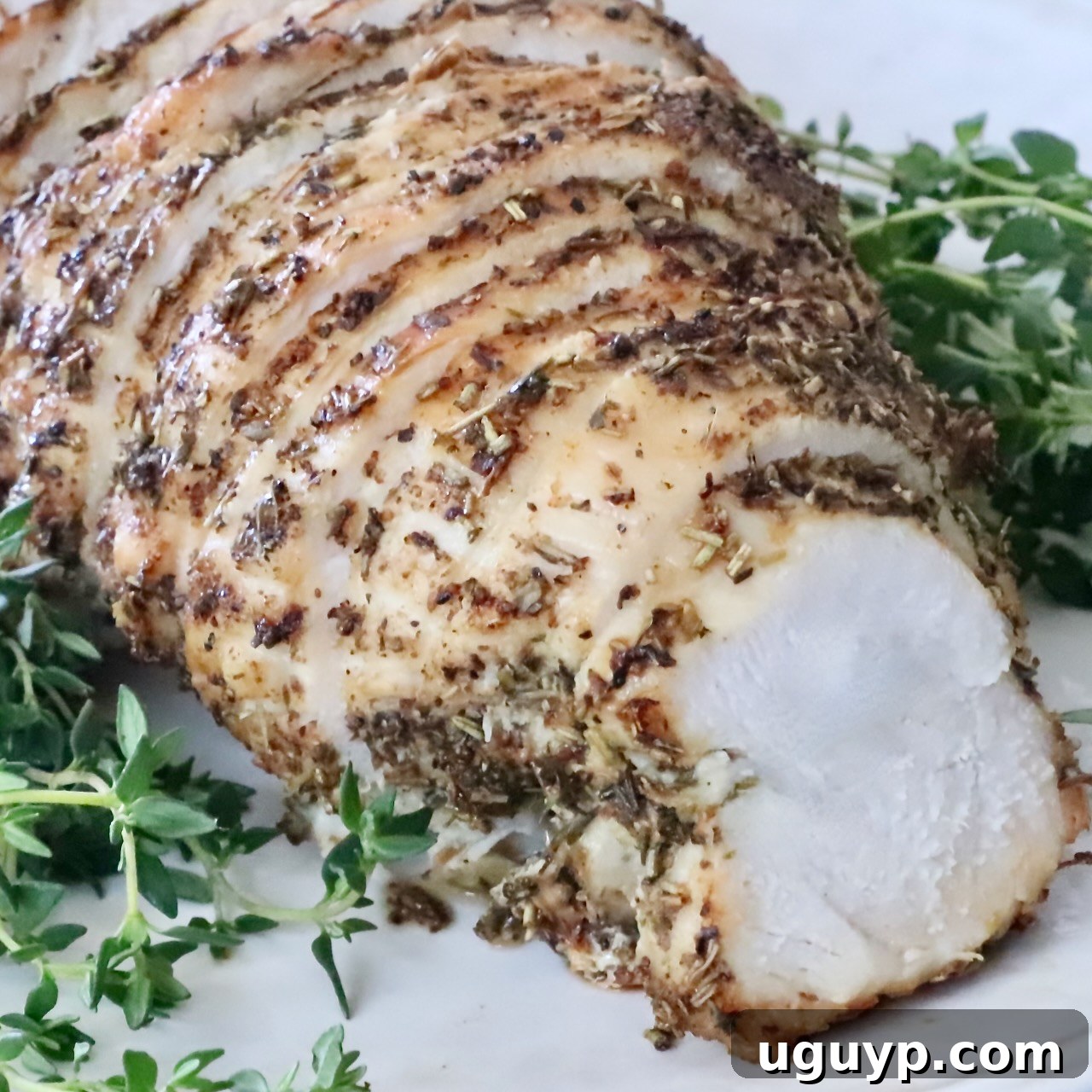 Sliced herb-crusted cooked turkey breast on a white plate