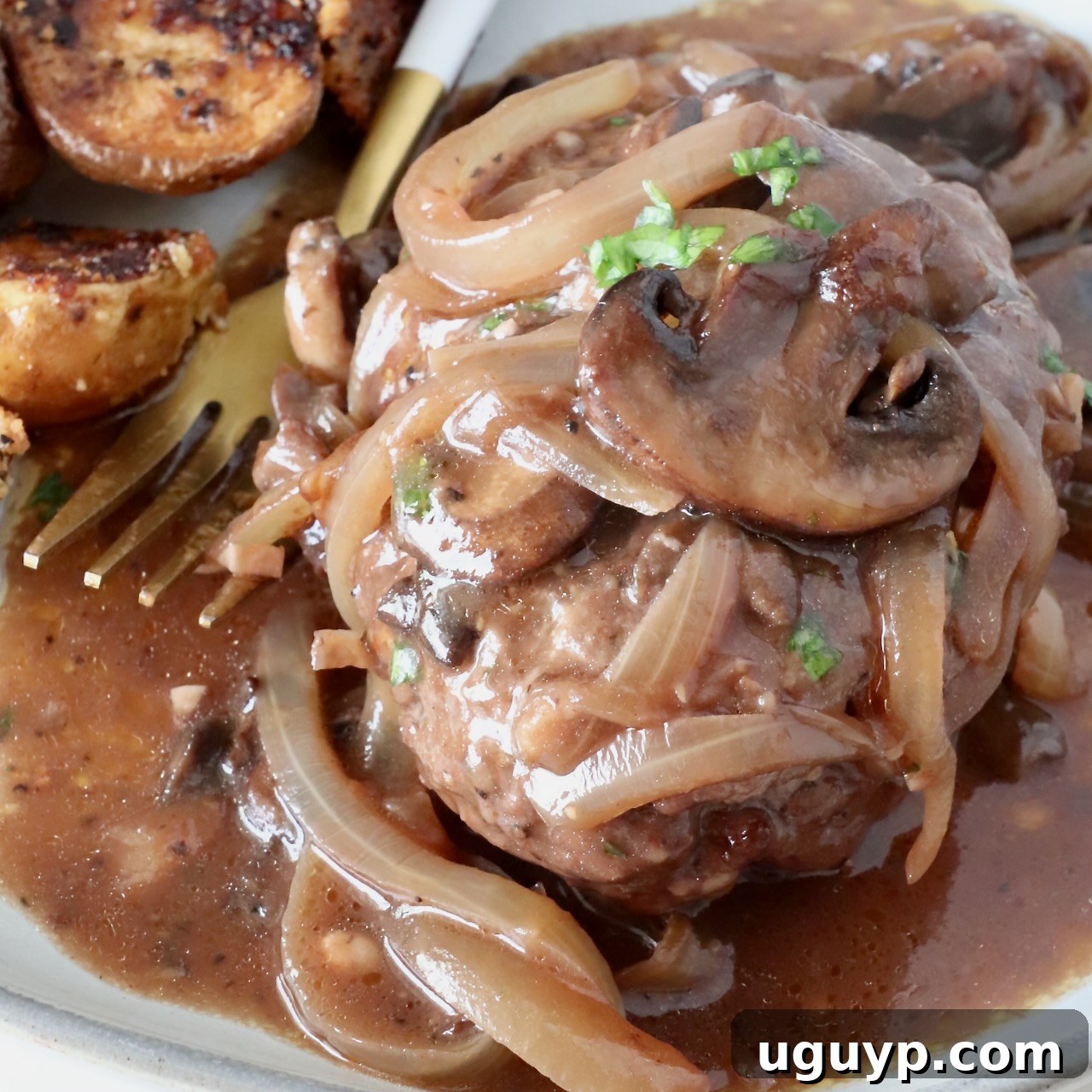 cooked chopped steak on a plate, covered with onions and mushrooms and gravy
