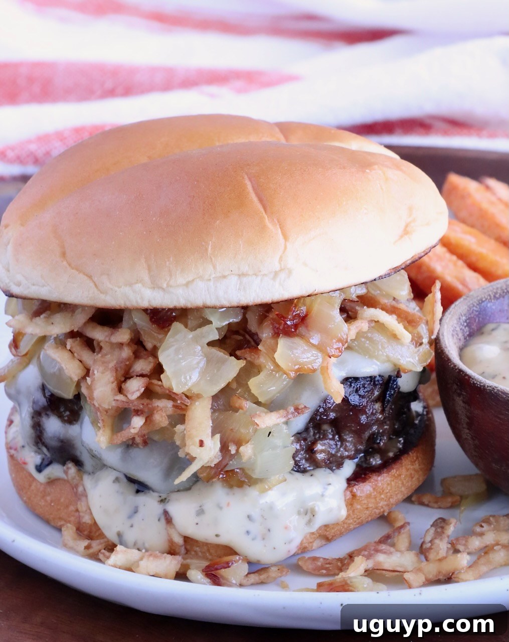 cheeseburger on a plate topped with caramelized onions and crispy fried onions, with a small bowl of sauce on the side