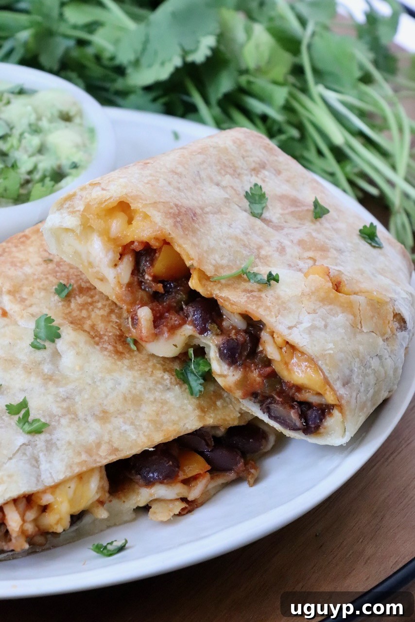 Cheesy Bean & Rice Burrito Recipe – Quick Weeknight Meal 2 bean and cheese burrito cut in half and stacked up on a plate with a bowl of guacamole and fresh cilantro in the background