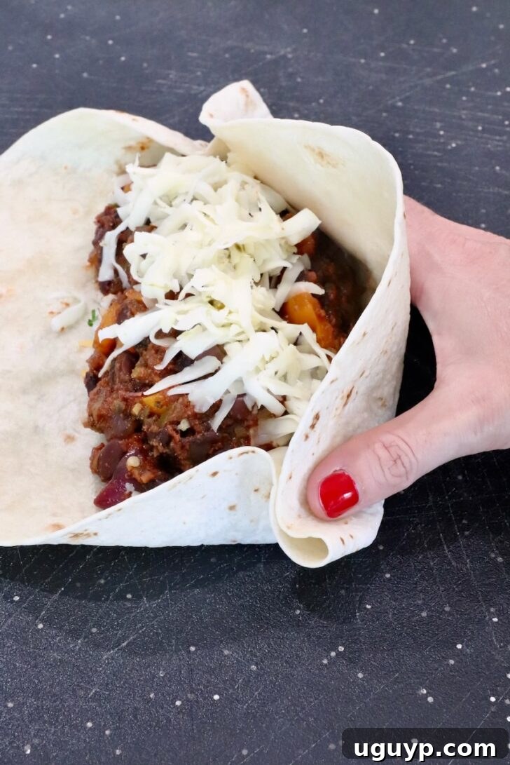 Cheesy Bean & Rice Burrito Recipe – Quick Weeknight Meal 12 hand folding a bean and cheese burrito on a cutting board