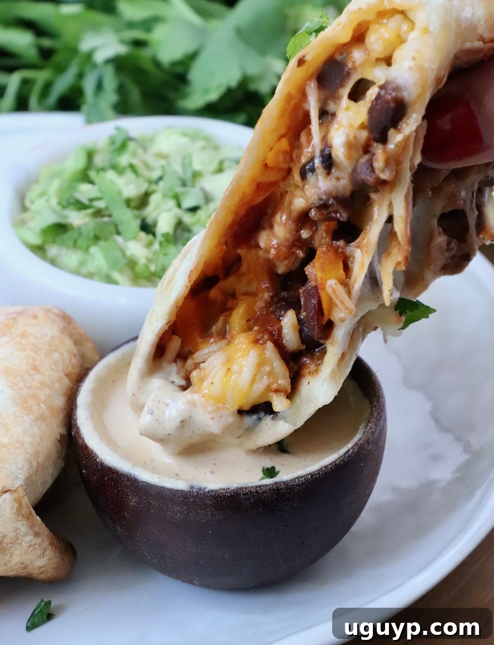Cheesy Bean & Rice Burrito Recipe – Quick Weeknight Meal 15 half of a burrito dipped into a small bowl of sauce with a bowl of guacamole in the background