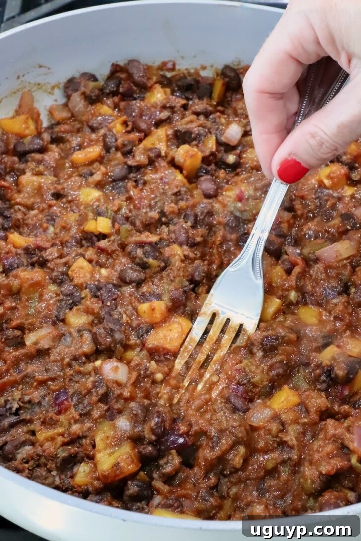 Cheesy Bean & Rice Burrito Recipe – Quick Weeknight Meal 7 bean burrito filling in a skillet with a fork smashing the beans