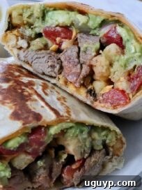 california burrito filled with carne asada and french fries cut in half and stacked up on a plate with a bowl of green salsa in the background