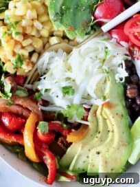 Zesty Chipotle Chicken Salad with Avocado 7 salad in a bowl topped with fajita veggies, avocado, corn, cheese, beans and tomatoes, with a fork in the middle of the bowl