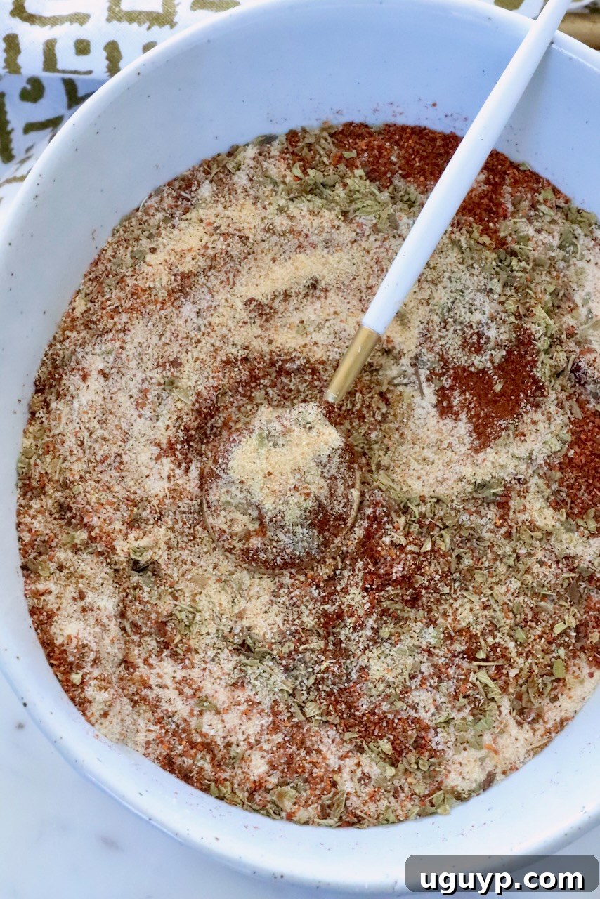 Authentic Mexican Barbacoa Seasoning Recipe 2 dried herbs and spices mixed together in a white bowl with a small spoon